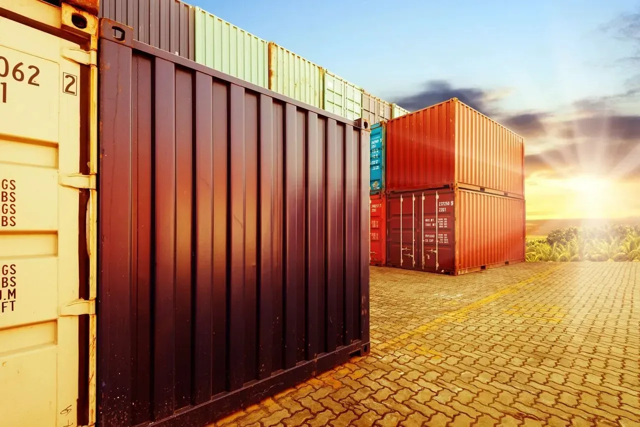 Row of shipping containers on a brick-paved yard at sunset.